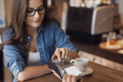 Young woman paying in cafe by credit card reader.