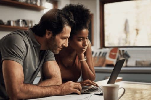 A couple shares a laptop that sits on a kitchen island next to paperwork.