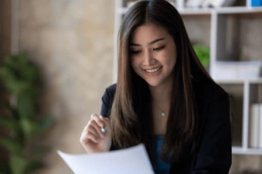 Woman sits at a desk while holding a pen and paper in her hands.