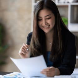 Woman sits at a desk while holding a pen and paper in her hands.