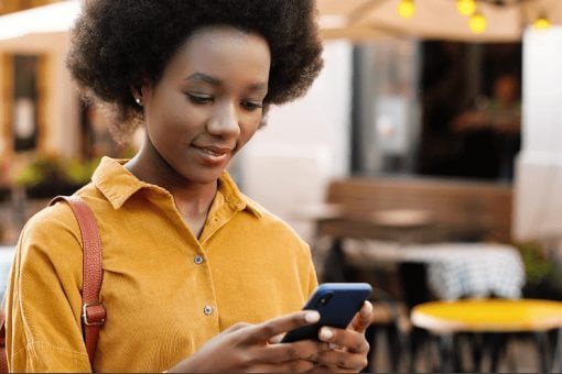 Woman standing outside of a restaurant looking at her phone.