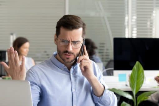 Man looking frustrated while talking on the phone and looking at his computer.
