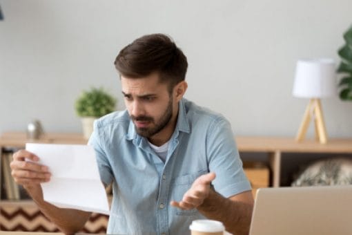 A young man stares in confusion at a credit card statement.