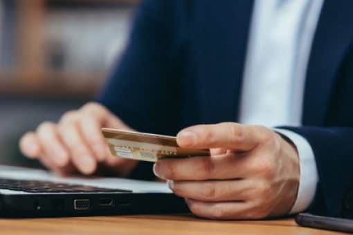 Man in suit holds credit card and types on laptop.