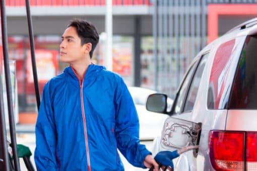 A man wearing a blue jacket filling fuel in his car at a gas pump.