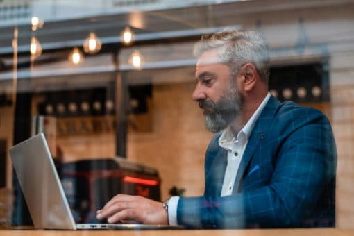 A man works on laptop near a cafe window.