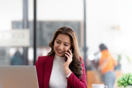 A woman talks on her cell phone while browsing on her laptop.