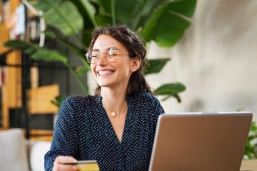 A smiling young woman holds a credit card while using a laptop.