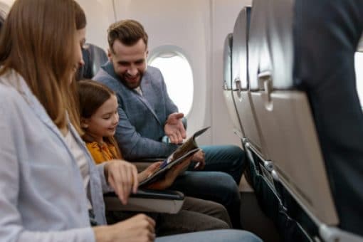 Man, woman, and child sit on a plane and look at a magazine together.