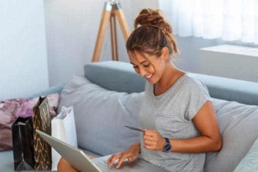 A woman is entering her credit card information into a laptop, while sitting on a couch.