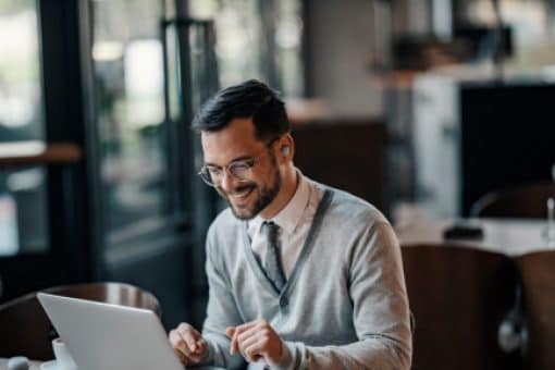 A young man sits in a coffee shop on his laptop.