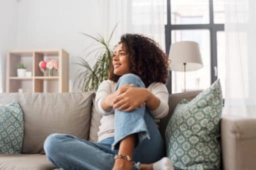 A happy woman sits on a couch in her home.