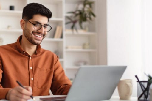 A smiling man with glasses studies his interest rates while sitting in front of his laptop.
