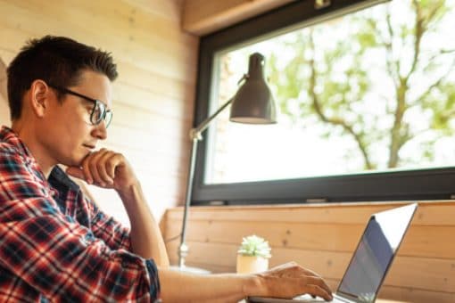 A young man contemplates as he browses on his laptop.