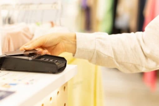 Hand taps credit card against pay terminal in clothing store.