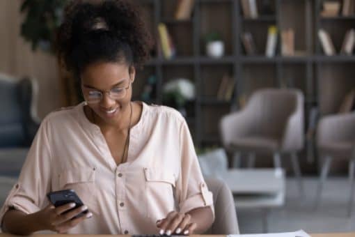 A smiling woman sits at a table and reviews her bills.