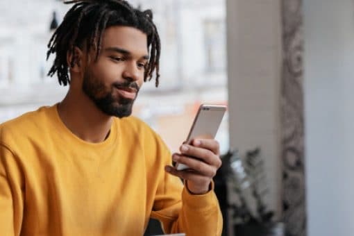 A young man looks contentedly at the phone in his hand.