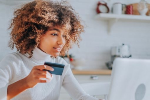 A woman refers to her credit card to enter numbers on her laptop.