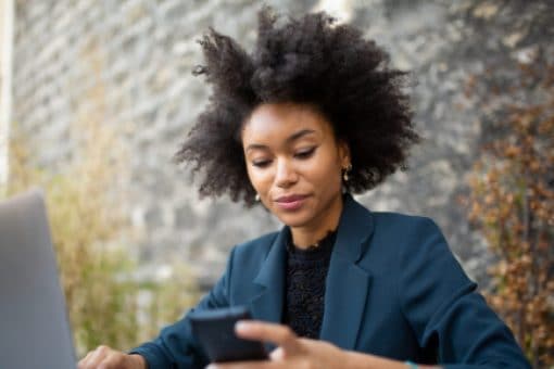 A professional woman sits in front of her laptop holding her cell phone.