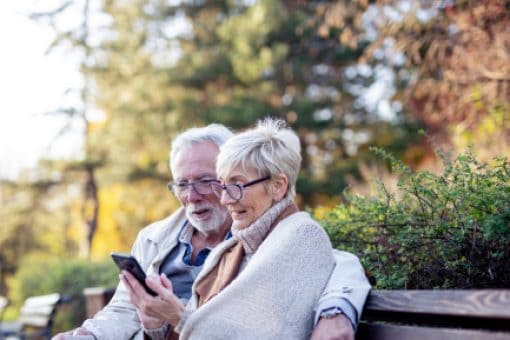 Couple sits on a park bench holding a credit card and staring at a cell phone.