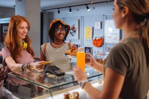 Two women standing in a bakery hand payment to the cashier.