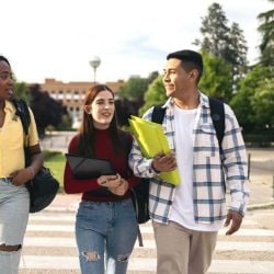 A group of three students with backpacks walks through a college campus.