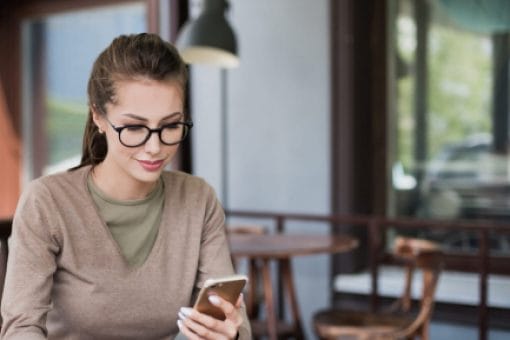 Woman sits at café table holding phone.