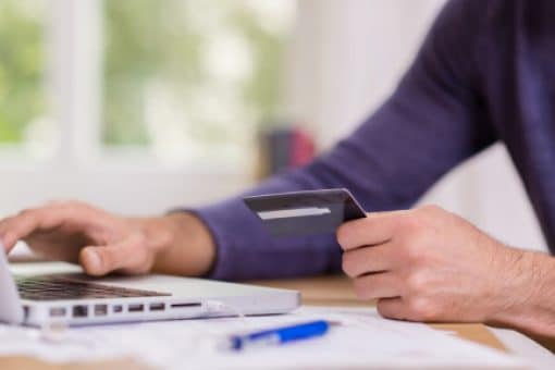 Man uses laptop and holds a credit card.