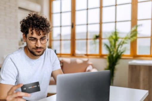 A man compares his Discover secured credit card with information on his laptop.