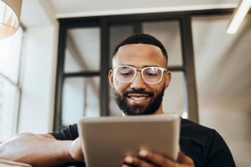 Man wearing glasses uses a tablet device in a well-lit room.