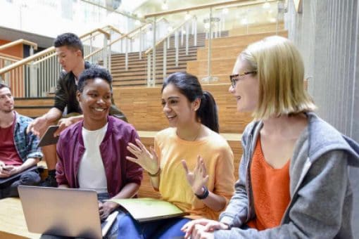 A group of smiling students sitting on a bench and talking to each other.