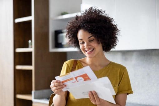 Happy woman smiling while looking at mail upon arriving home.