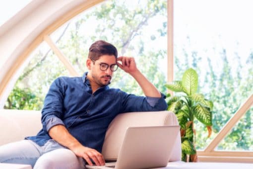Professional man sits on his couch and looks at his laptop.
