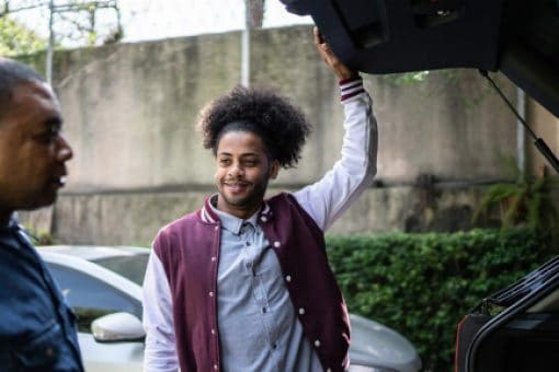 A smiling young man holds the liftgate of a car open as an older man looks on.