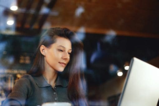 Looking through cafe window at woman working on laptop.