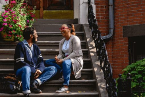 Two people sitting on the outdoor steps of a brick building talking and smiling.