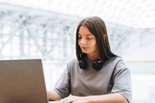A dark-haired woman is sitting at a table while browsing on a laptop.