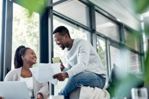 Happy couple sits at home looking at paperwork and laptop computer.