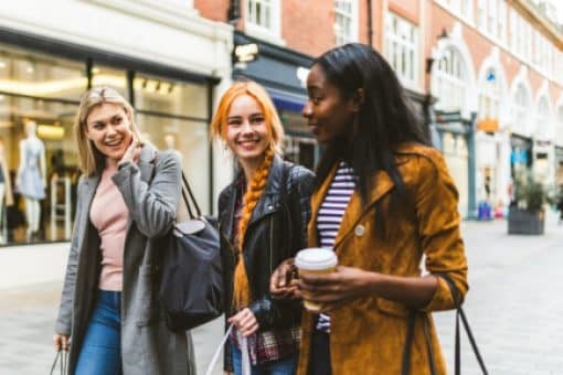 Three women holding shopping bags walk while talking outside.