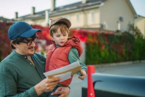 A father collects mail from the mailbox with his young son.