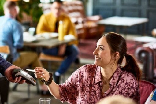 A woman using contactless payment with a credit card to pay at a restaurant.