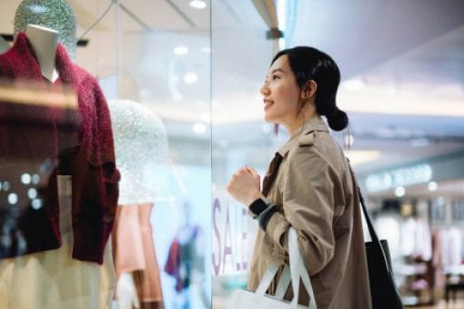 A woman in a mall admiring a dress displayed in a shop window.