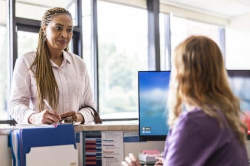 A woman stands at a hospital reception desk writing on paper.
