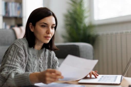 A woman sitting in sitting in their living room and reviewing some paperwork.
