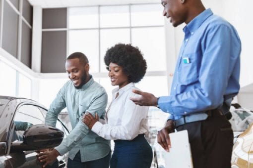 A couple looks at a car they want to lease as a salesman stands by them.