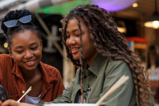 Two friends sitting in a café, one showing something on her phone to the other.