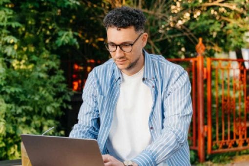 A man sitting outdoors and working on his laptop.