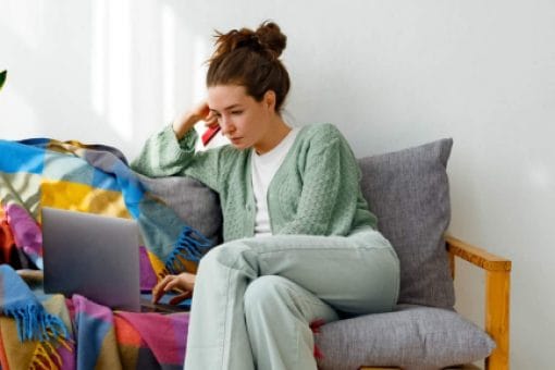 A woman sitting on the couch, looking down at her laptop.