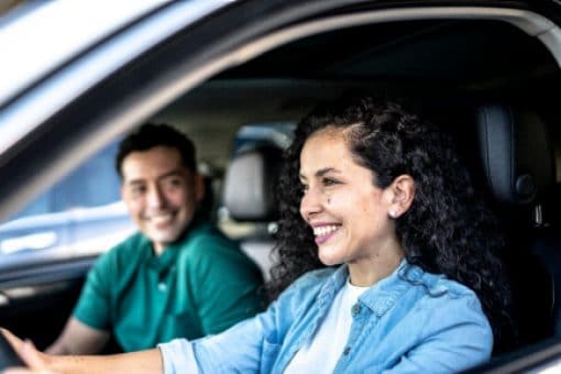 Woman driving a car with man in the passenger seat, both smiling 