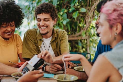 A man sits with his friends and uses his credit card at an outdoor restaurant to pay the server.
